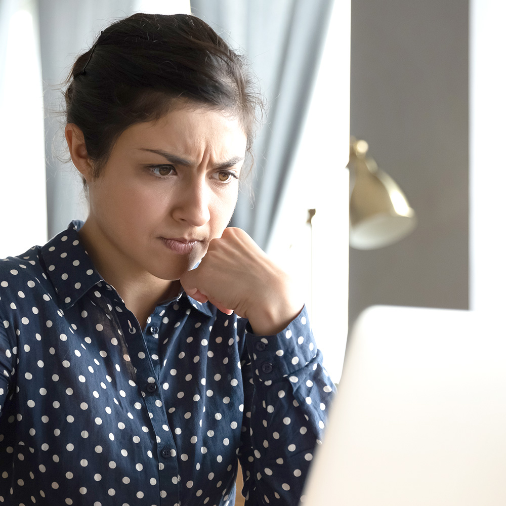 Das Bild zeigt eine Frau, die konzentriert vor einem Computerbildschirm sitzt und Konzentrationsfalten auf der Stirkn hat, die oft als Zornesfalten bezeichnet werden. 